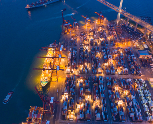 Aerial top view of container cargo ship in the export and import business and logistics international goods in urban city. Shipping to the harbor by crane in Victoria Harbour, Hong Kong City at night.